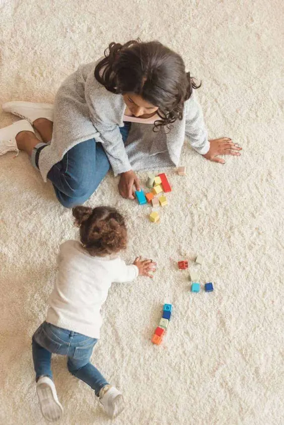 A mother and her little toddler playing together with colorful building blocks