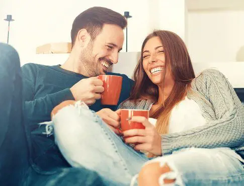 Couple having a laugh during their coffee conversation while sitting on a couch. 